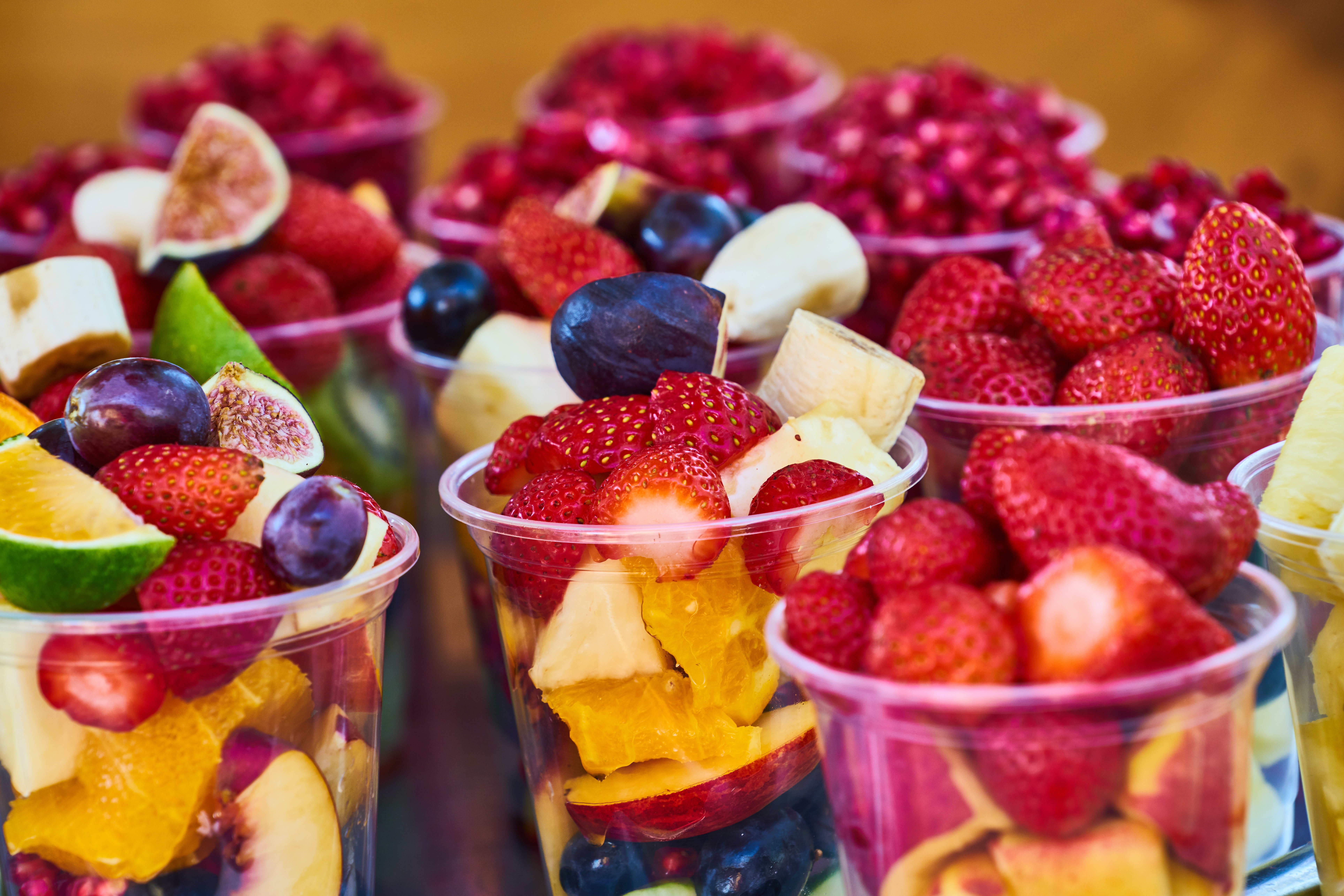 Nine clear plastic cups filled with bight summer fruit pieces with strawberries and blueberries on top